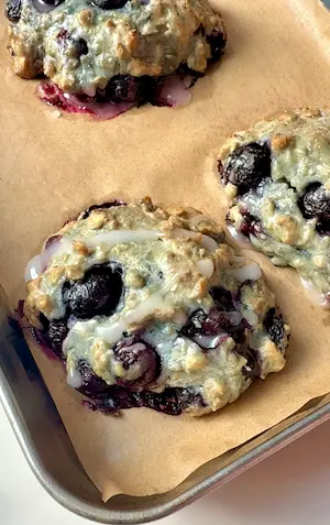 Blueberry fritters on parchment paper in a baking tray with white glaze drizzled on top