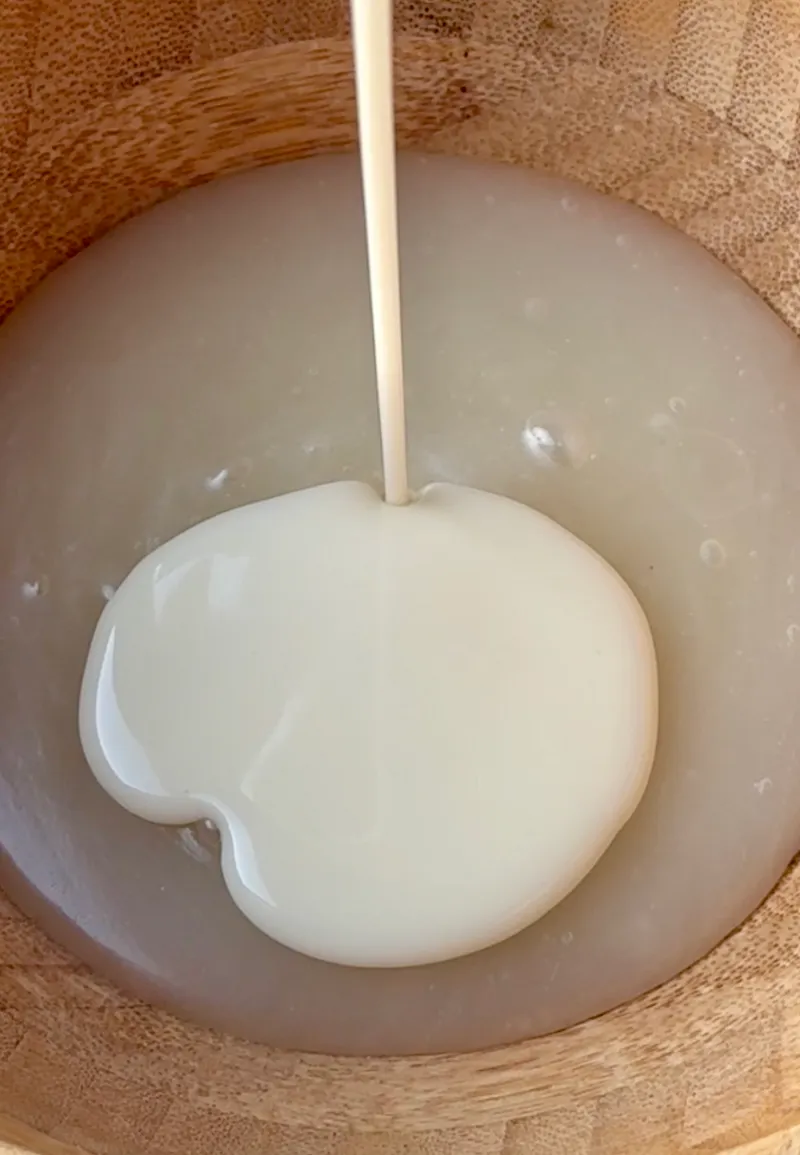 Condensed coconut milk being poured into a wooden bowl with the melted coconut butter