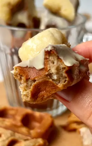 A hand holding a gluten free banana bread waffle stick broken in half showing the fluffy interior with white chocolate dripping down
