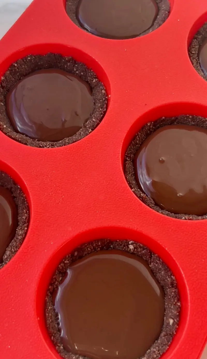 Multiple hot chocolate fudge cups filled with glossy chocolate ganache in a red silicone muffin mould ready to set in the freezer