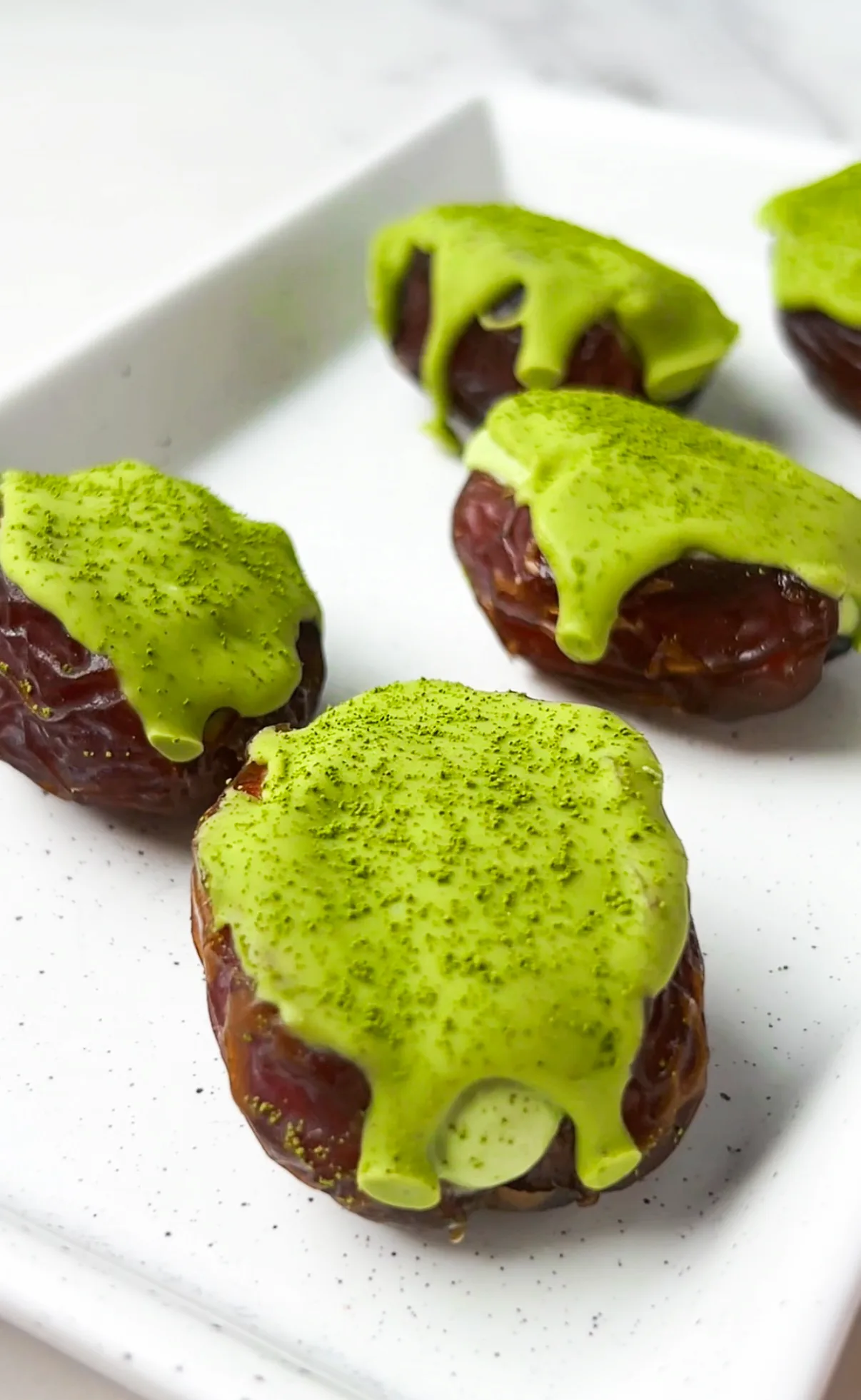 Matcha cheesecake stuffed medjool dates drizzled with matcha white chocolate on a white plate