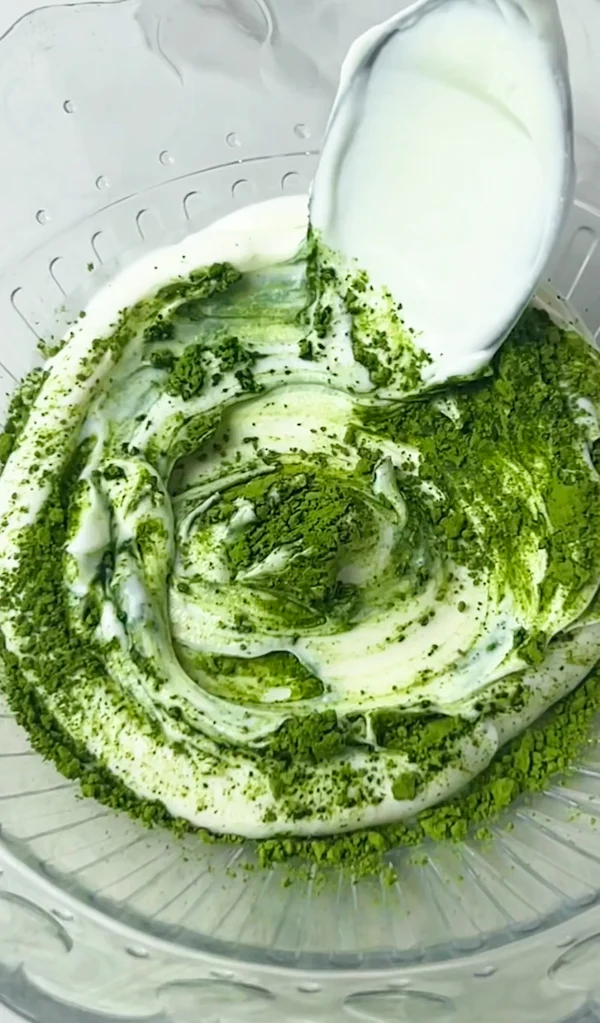 Step 1: Matcha powder being mixed into thick Greek yogurt in a bowl
