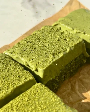 No bake matcha ganache bars cut into squares on parchment paper showing the bright green ganache top and darker green chewy base shot from above