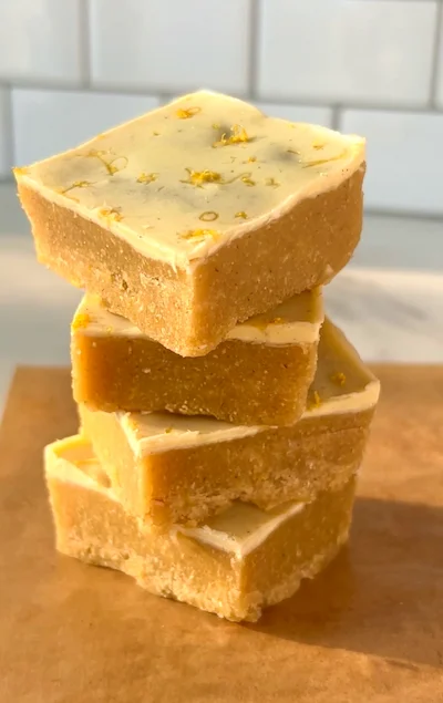 A stack of no-bake lemon bars with a creamy white chocolate lemon top and golden almond base garnished with lemon zest