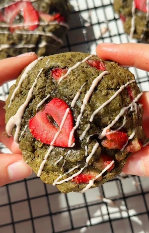 Gooey strawberry matcha cookies topped with fresh strawberry slices on parchment paper