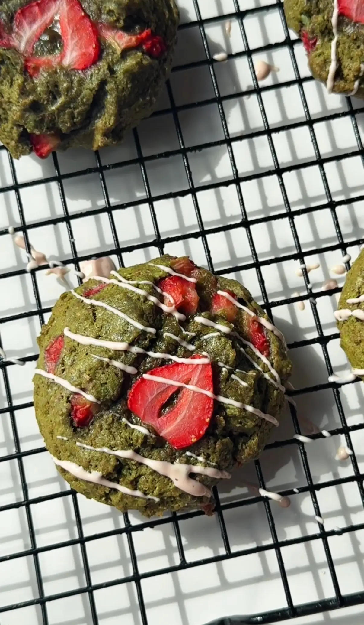 Gooey strawberry matcha cookies on parchment paper showing the green matcha cookie base topped with fresh strawberry slices