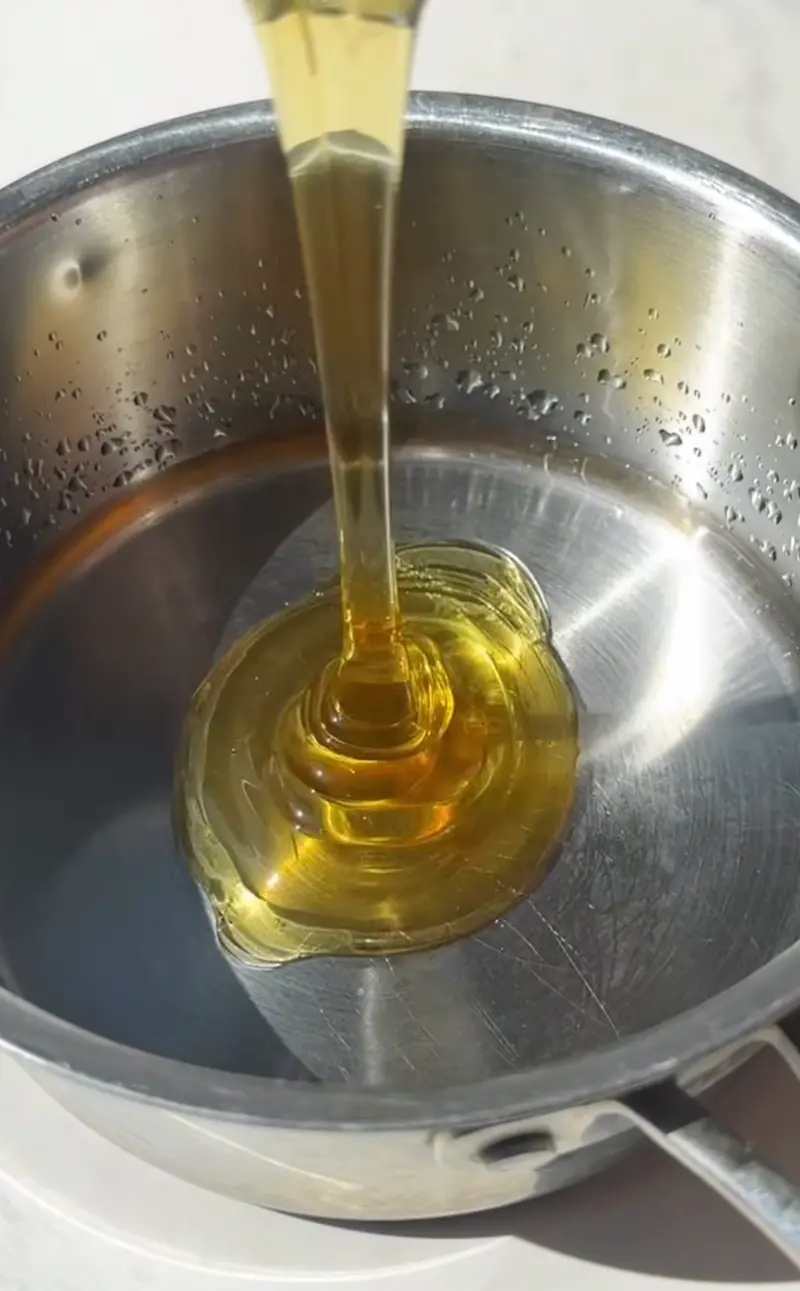 Golden maple syrup being poured into a small stainless steel saucepan