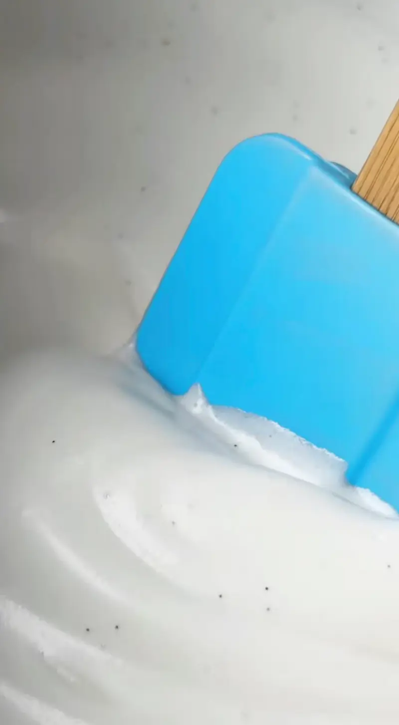 A blue silicone spatula folding thick white vanilla marshmallow fluff in a mixing bowl